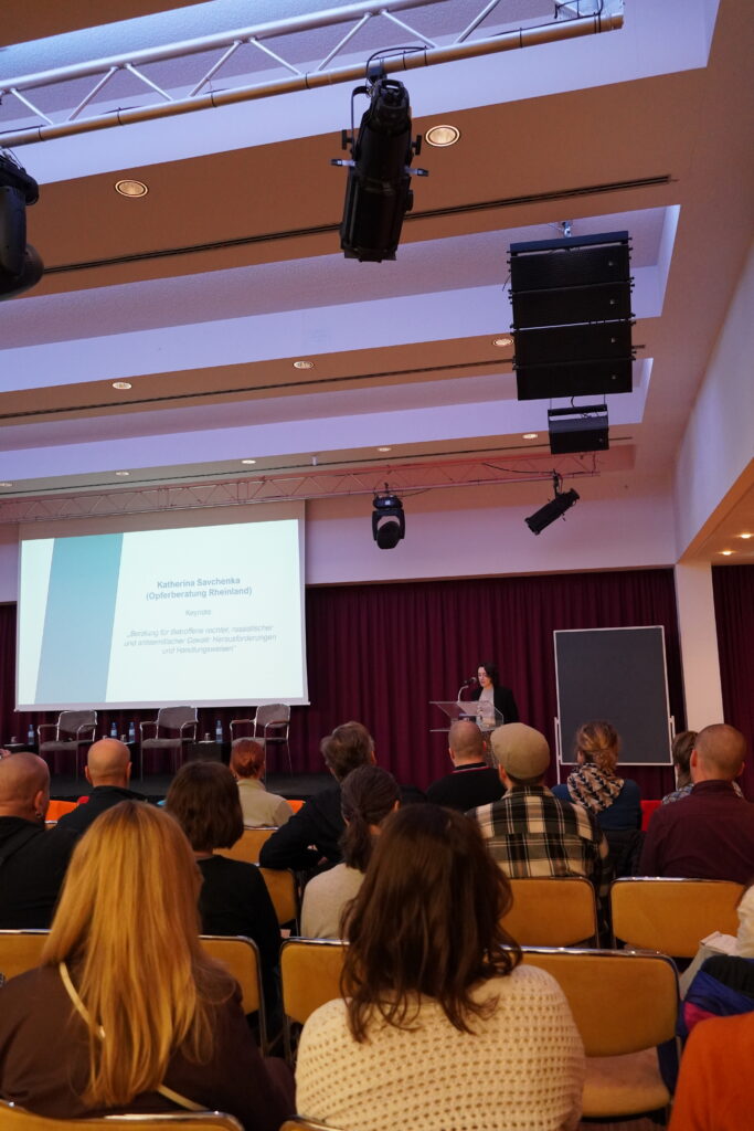 Vortragssaal mit Publikum, Referentin am Pult und Projektionsleinwand mit Präsentation.
