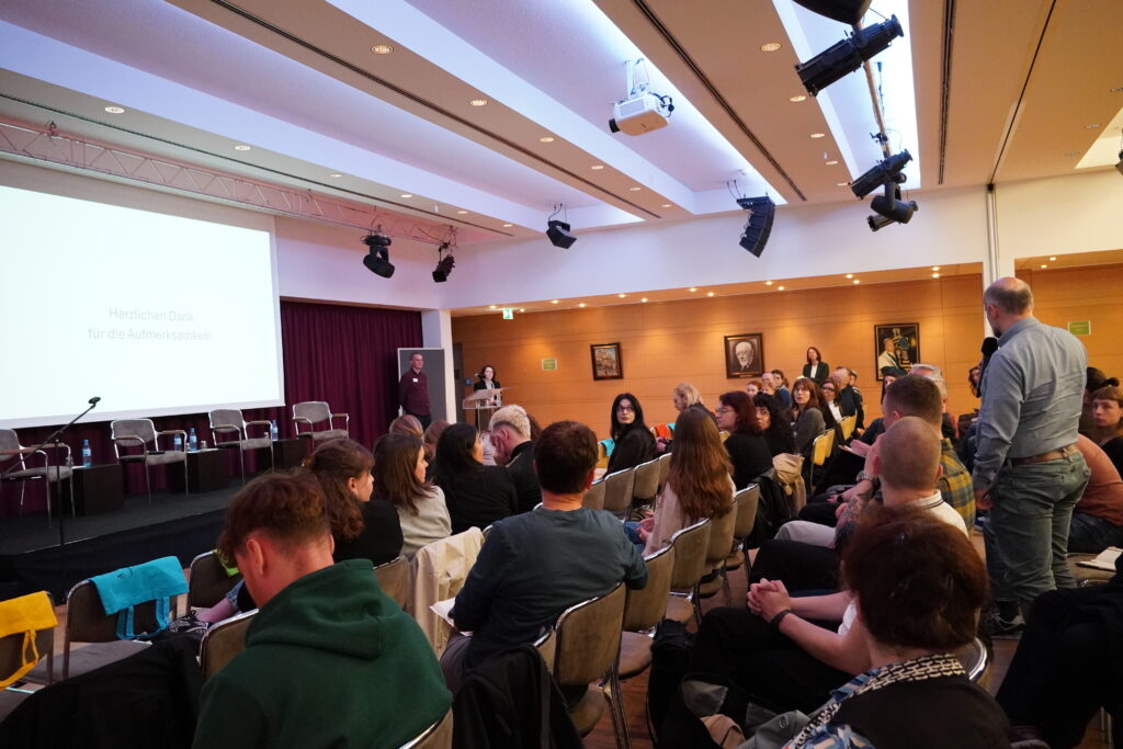 Publikum in einem Vortragssaal; auf der Leinwand steht Herzlichen Dank für die Aufmerksamkeit.
