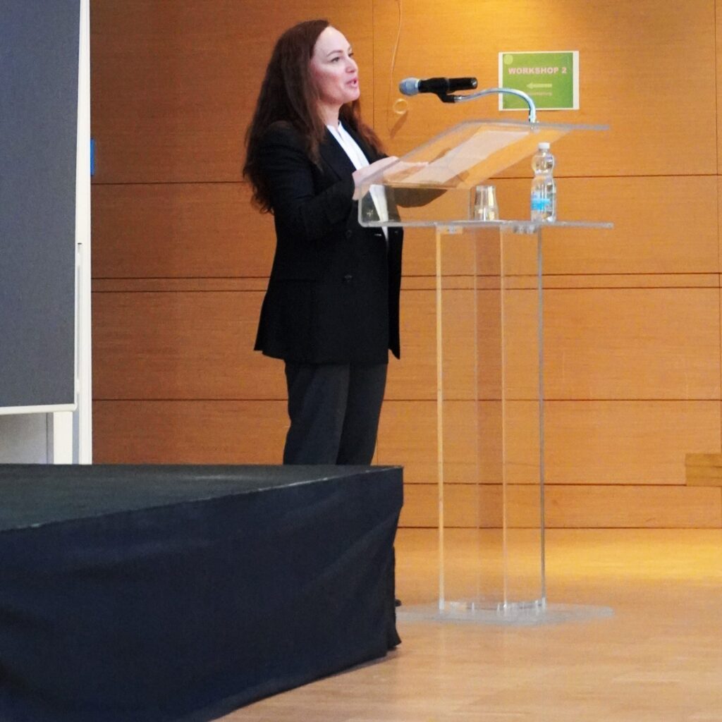 Frau im schwarzen Anzug spricht am Rednerpult mit Mikrofon bei einem Workshop.