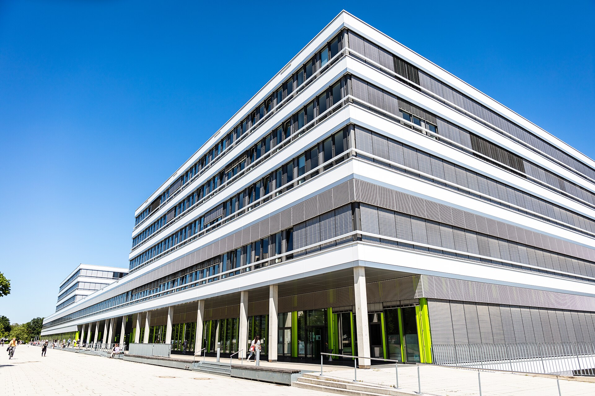 Modernes Bürogebäude mit weißen Fassadenlinien vor blauem Himmel, mit Menschen auf dem Vorplatz